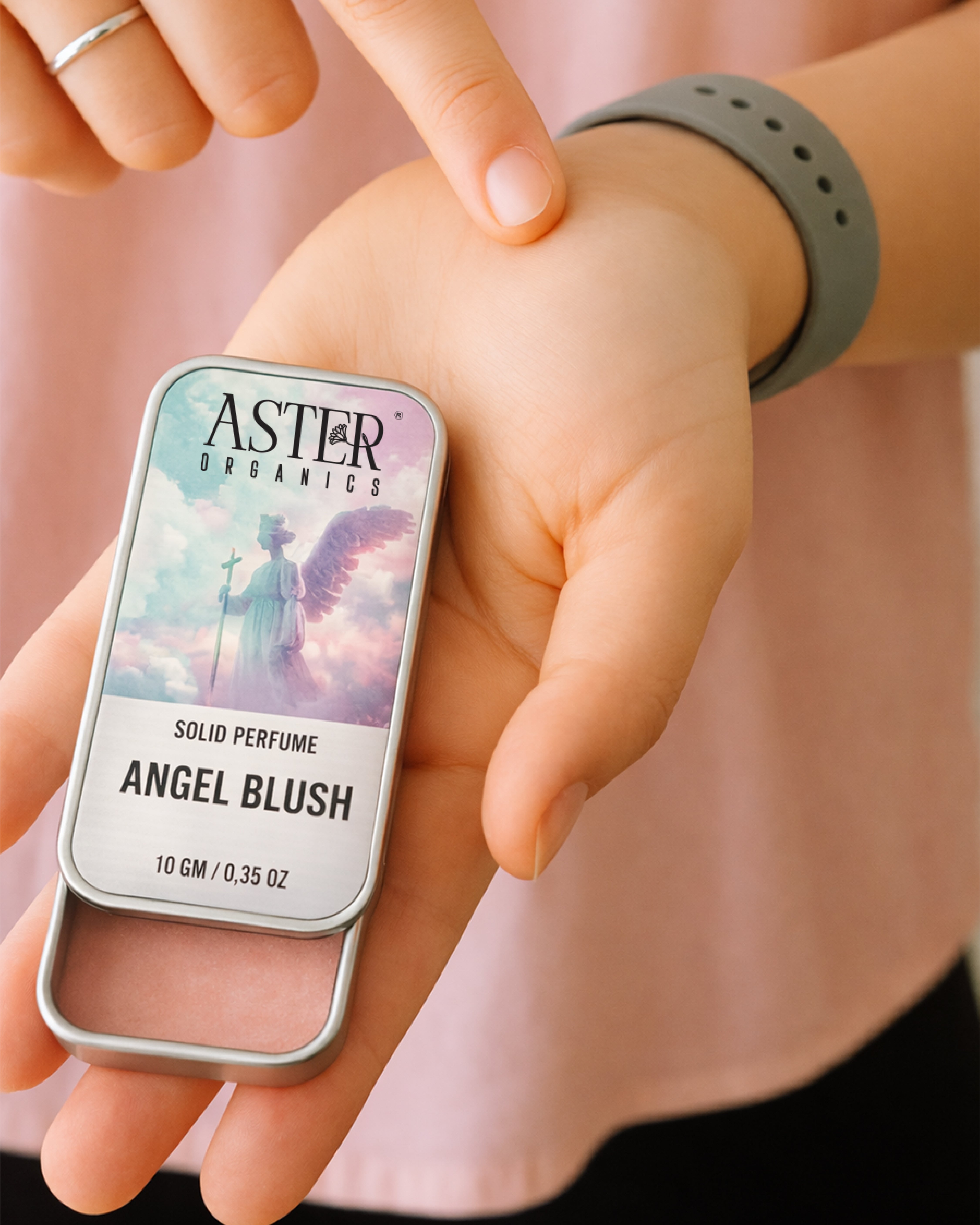 Hand holding a solid perfume packaging labeled 'Angel Blush' by Aster Organics.