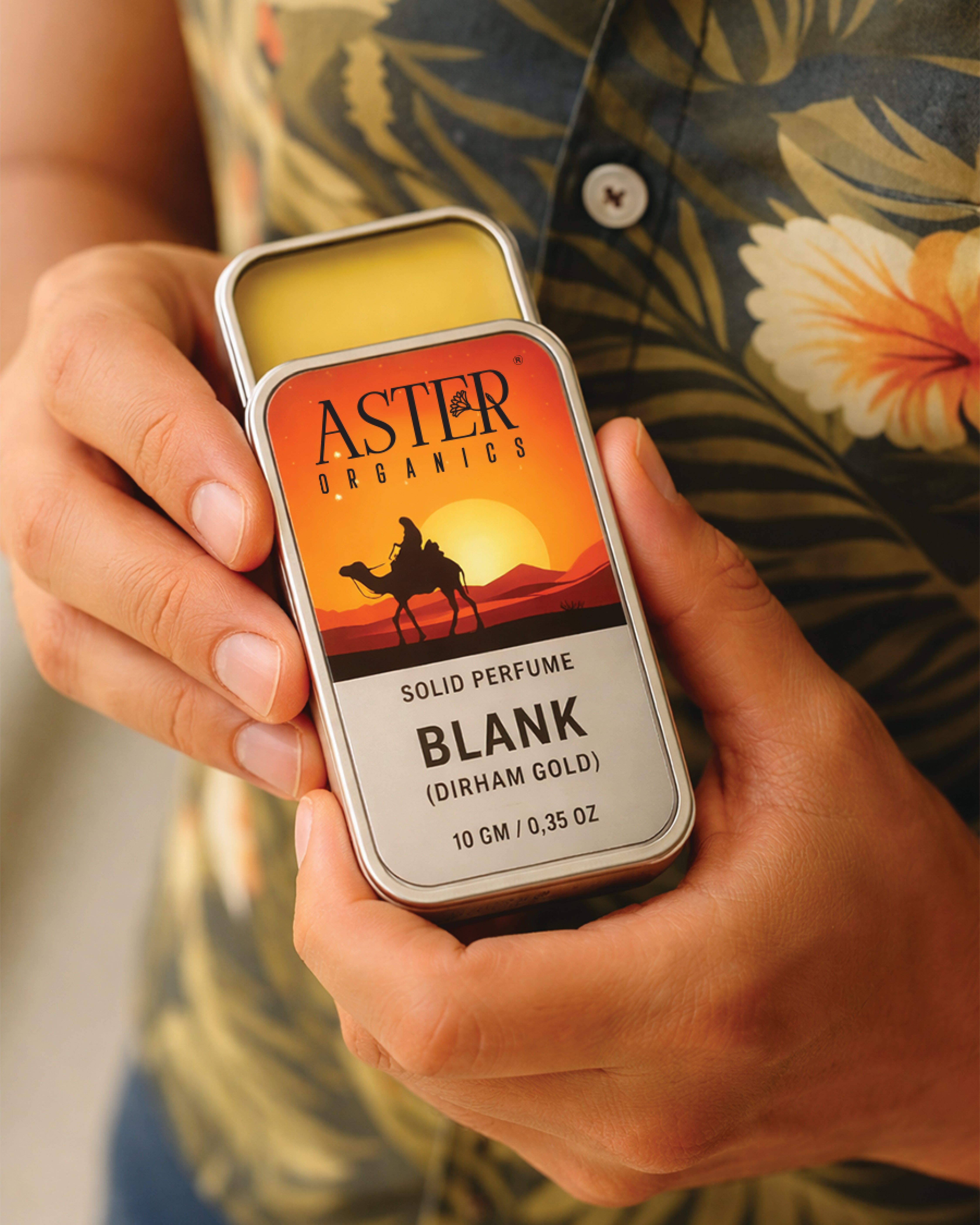 Person holding a tin of Aster Organics solid perfume with a desert design.