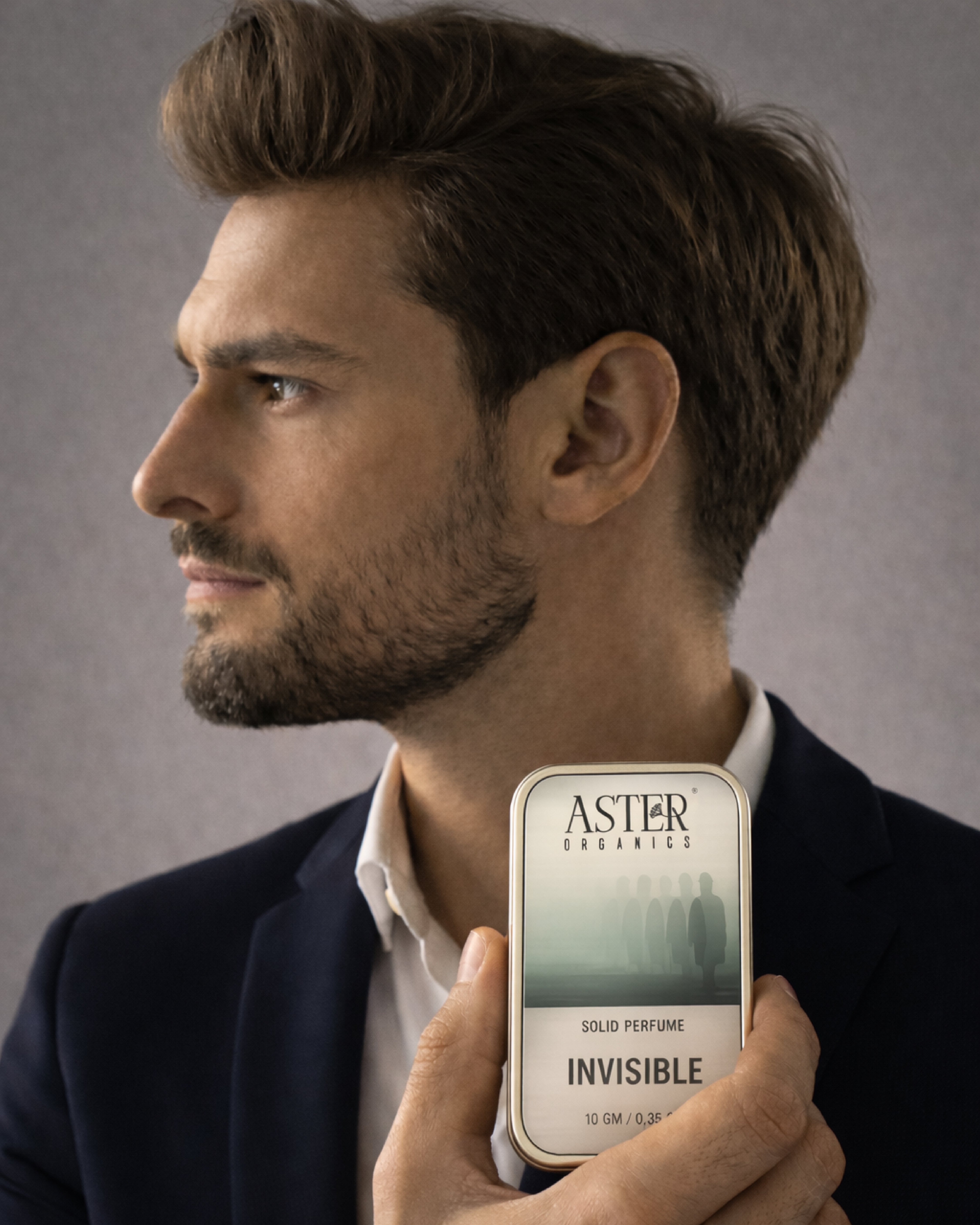 Man holding an Aster & Chessel solid perfume in front of a gray background